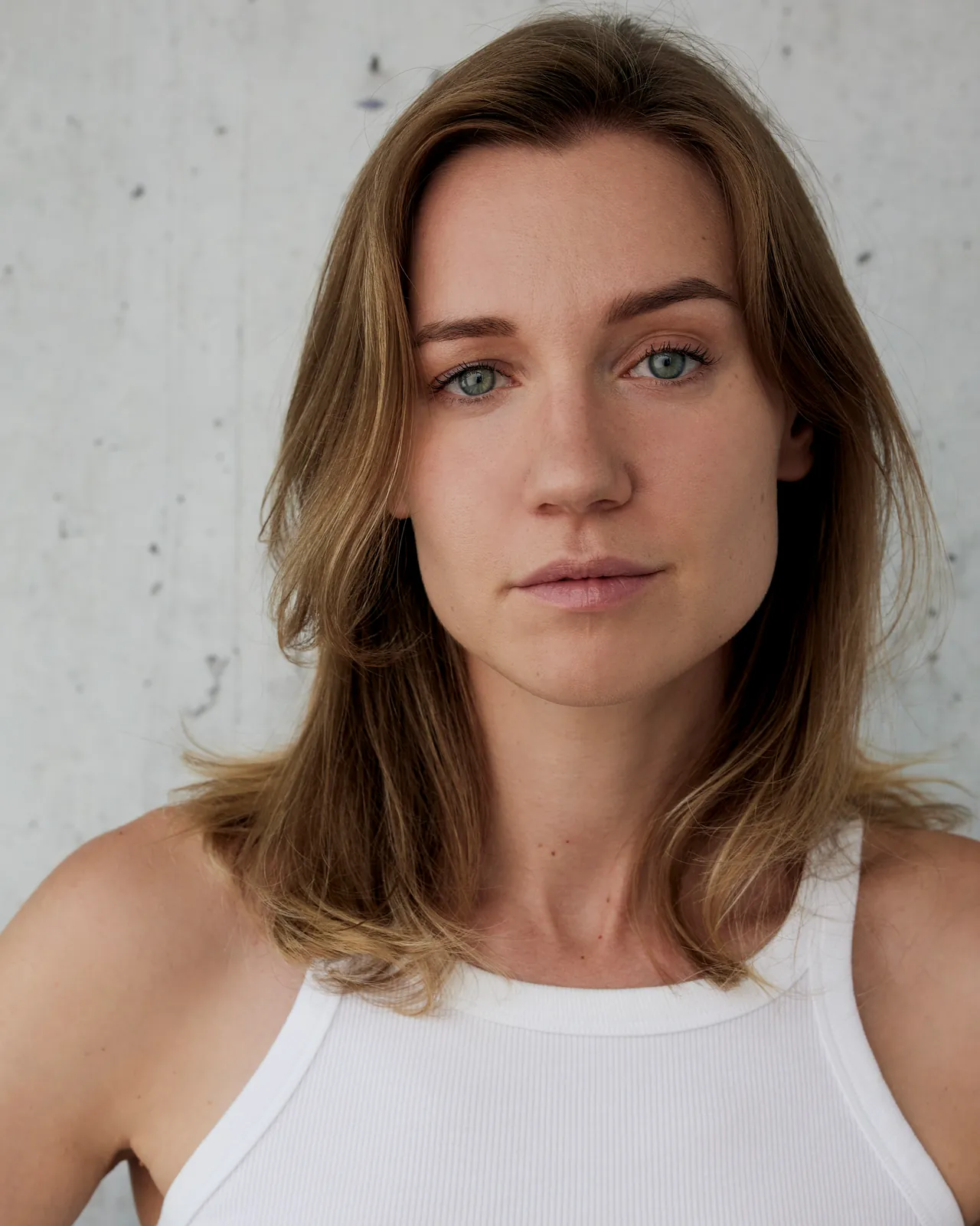 Ania Nova headshot in a white tank top against a concrete wall